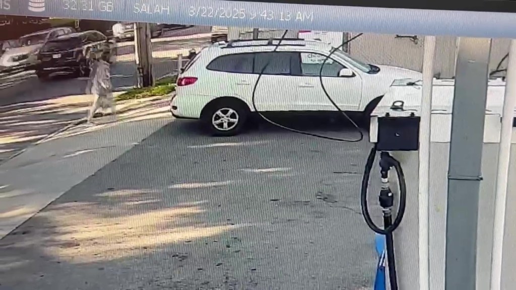 Surveillance video still image of a person near a white SUV at a gas station.