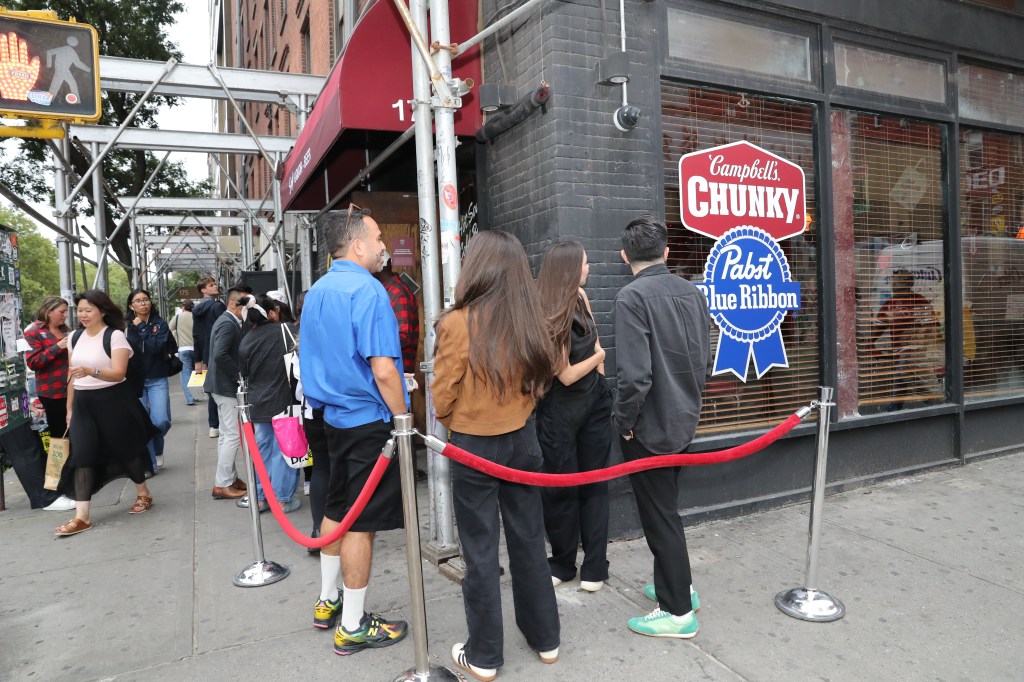 People waiting in line outside a bar with Campbell's Chunky Soup and Pabst Blue Ribbon signage.
