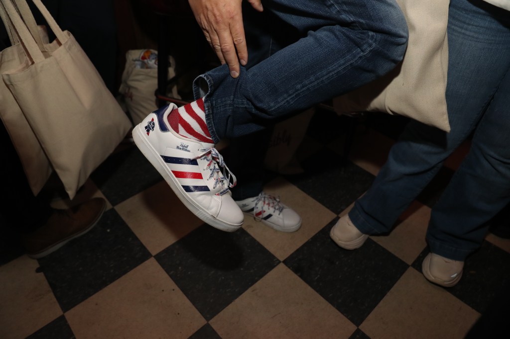 Person wearing Pabst Blue Ribbon sneakers and red and white striped socks.