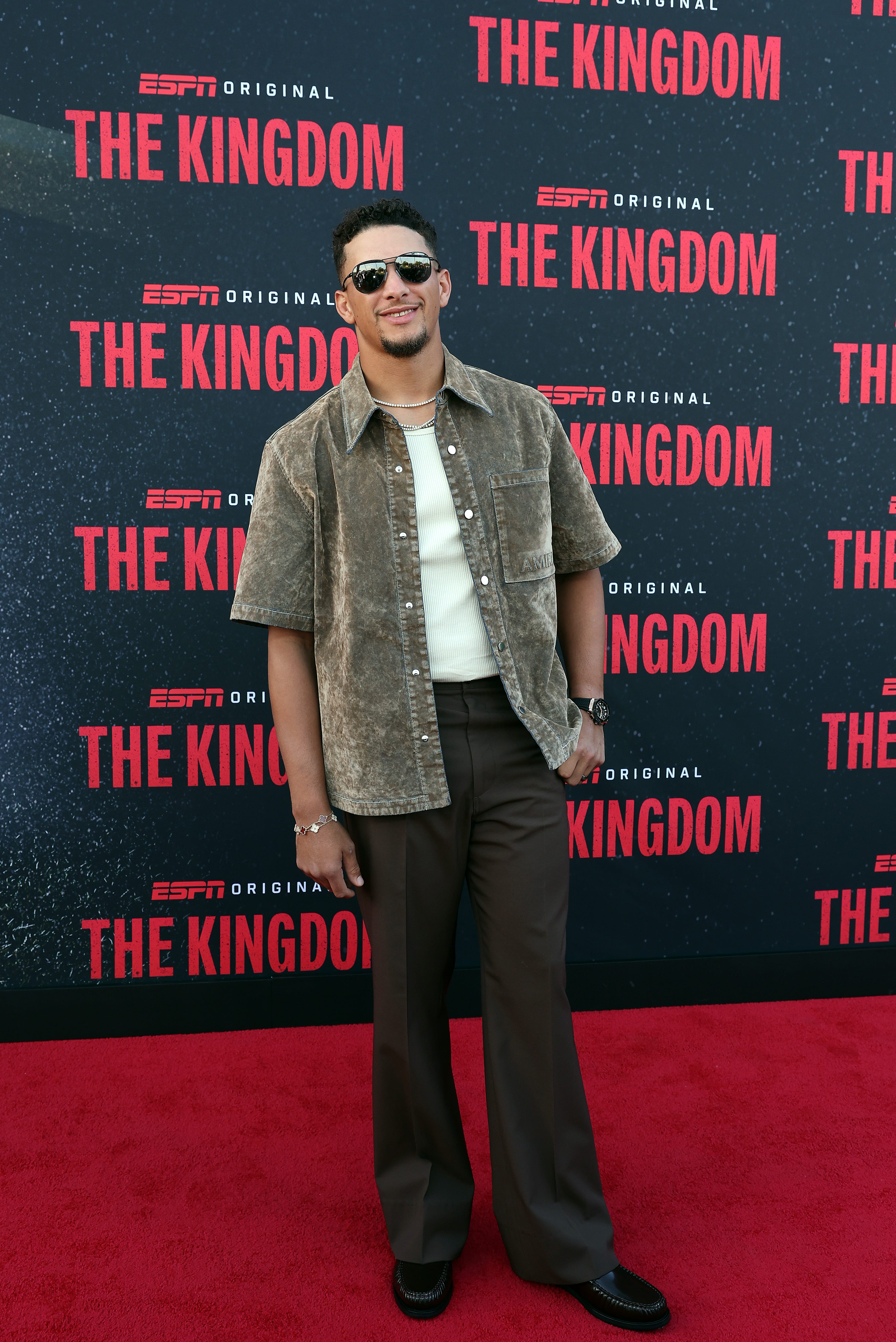 Patrick Mahomes wears sunglasses and poses on a red carpet for a screening of "The Kingdom."