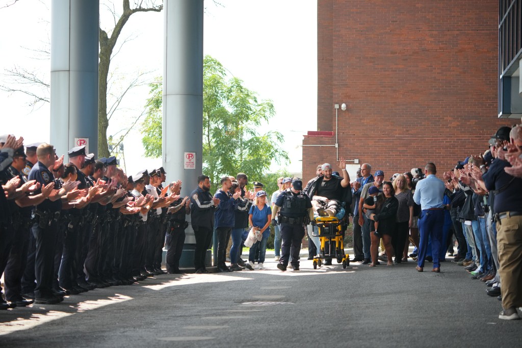 NYPD officers applaud as a wounded detective is released from the hospital.