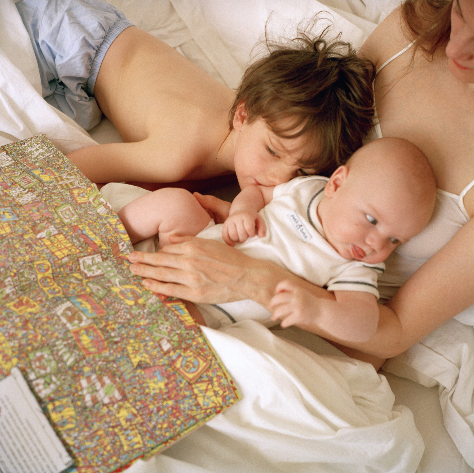 A toddler and baby lay in their mother's lap while she reads a book