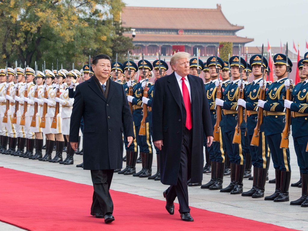 Xi Jinping and Donald Trump walking on a red carpet with a military honor guard.