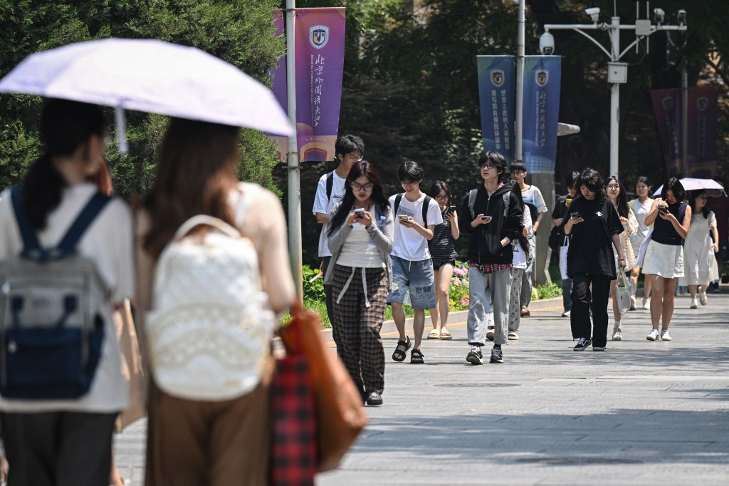Students walking on a university campus, looking at their phones.