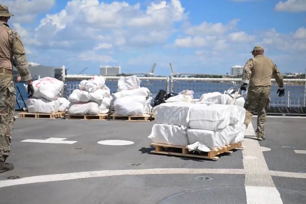 Coast Guard members moving bales of confiscated drugs on a ship's deck.