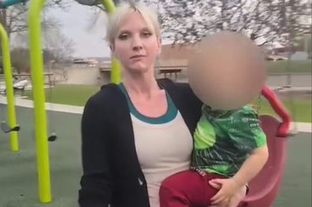 Woman holding a child at a playground.  Child's face is blurred.
