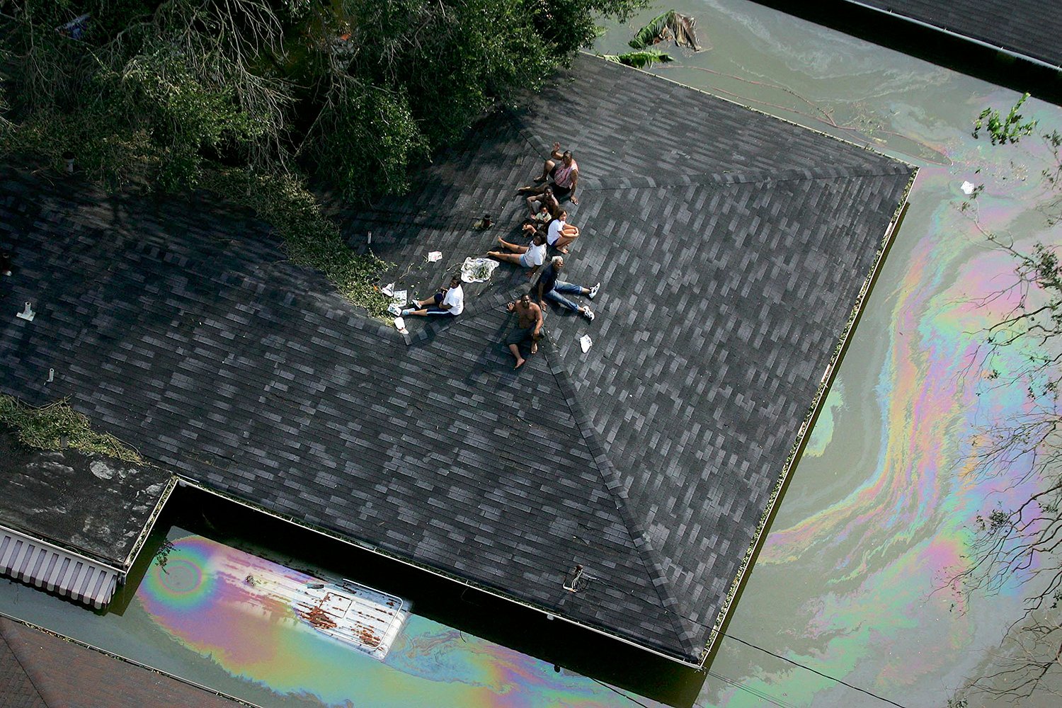 An aerial view shows several people stranded amid floodwaters on the roof of a house.
