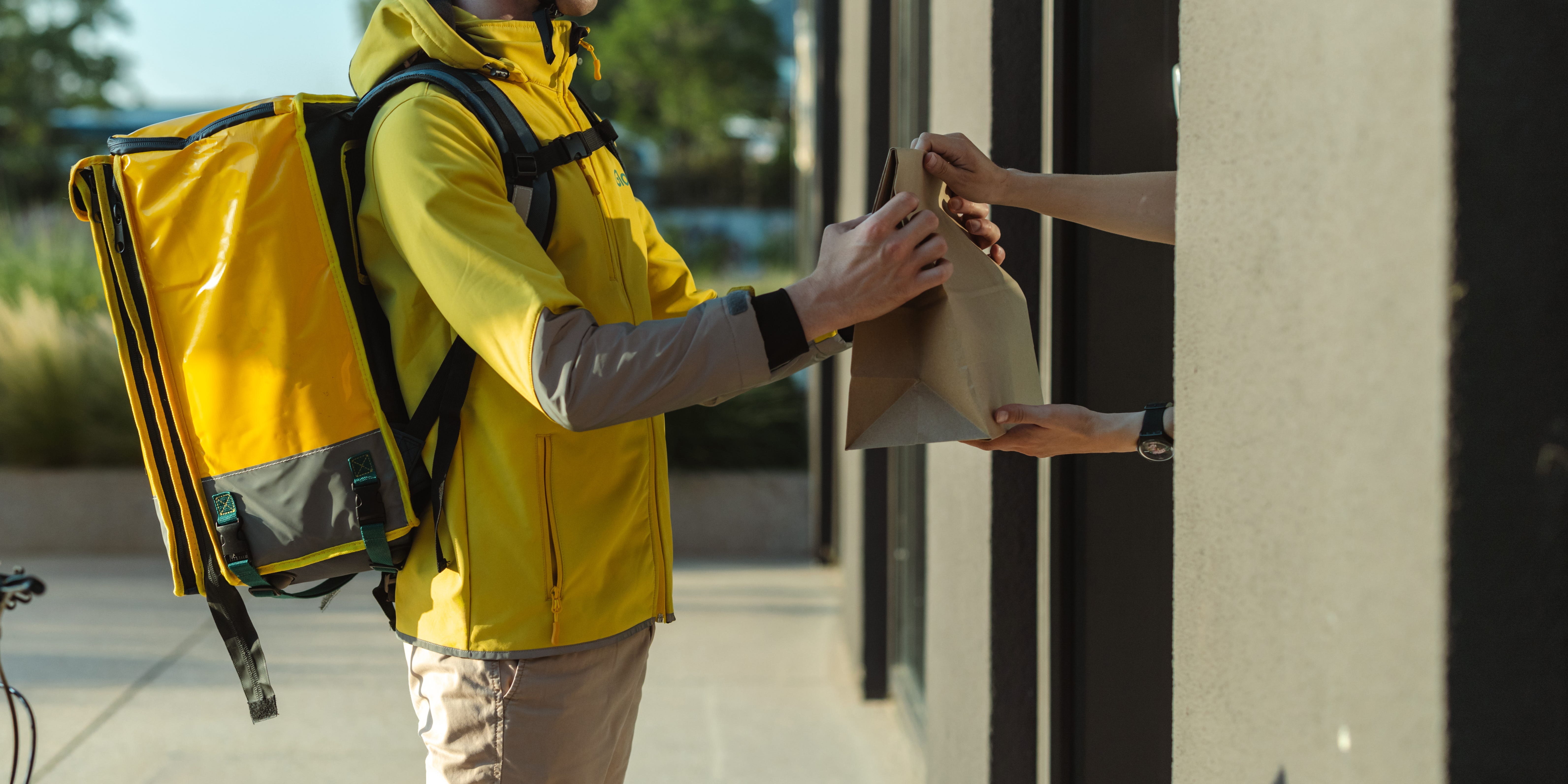 A person in a yellow jacket and a backpack delivering food via bicycle