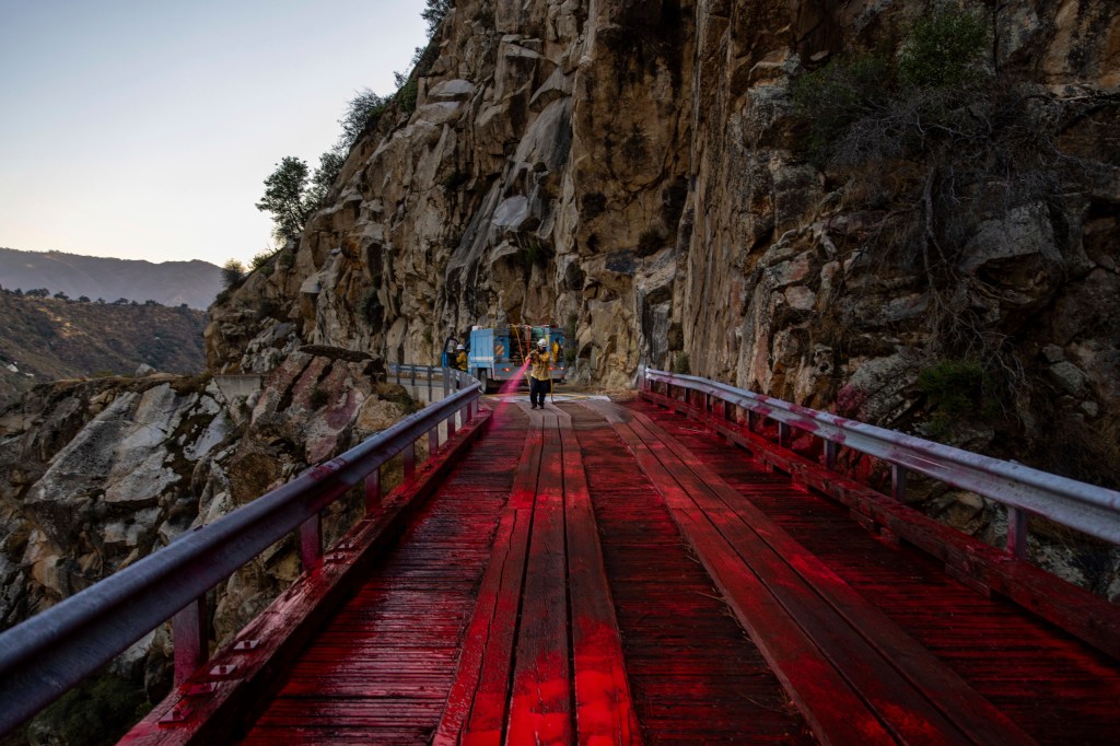 Firefighters spraying fire retardant on a bridge during a wildfire.