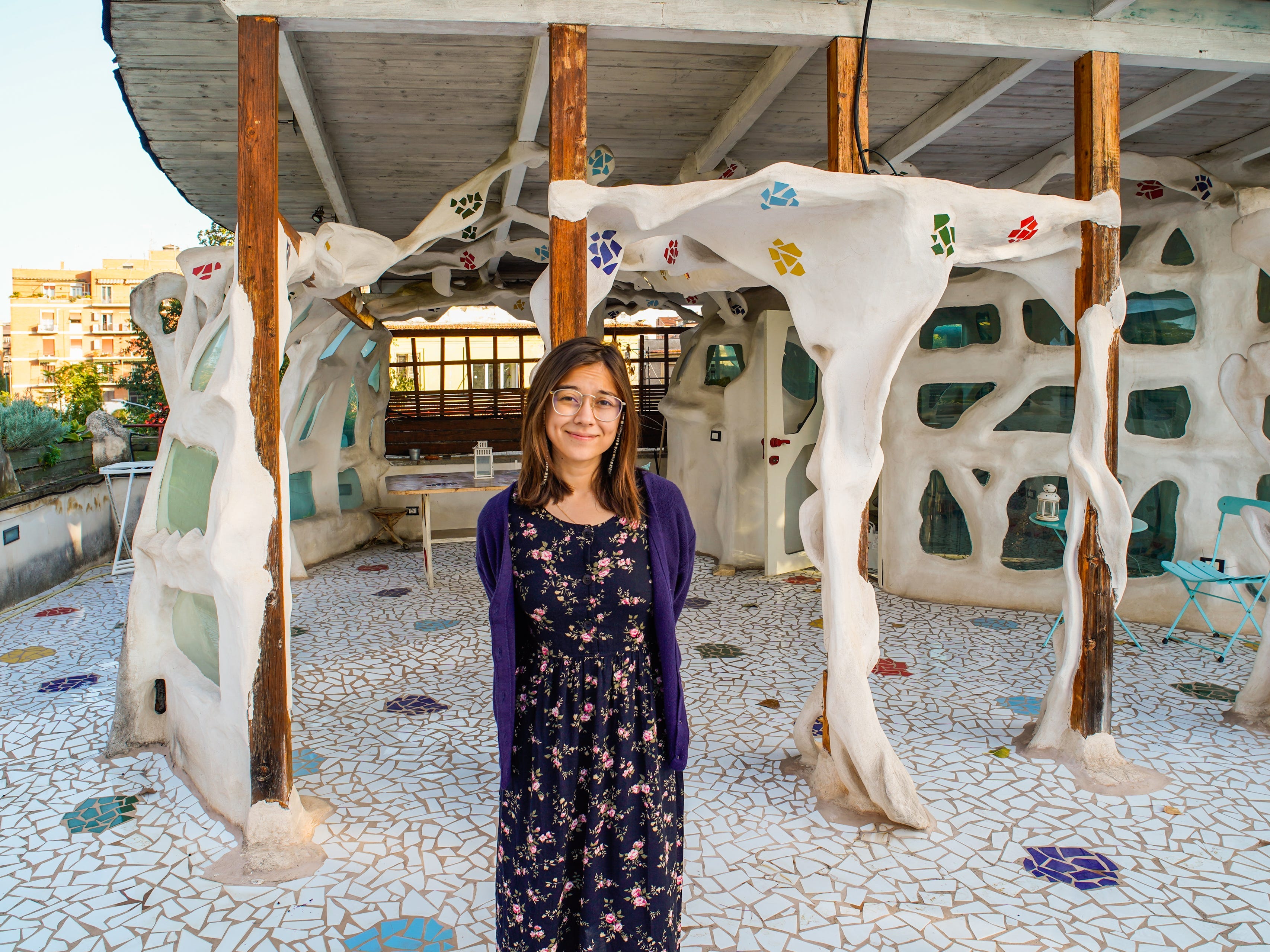 The author stands on a colorful patio in front of the sculpture home