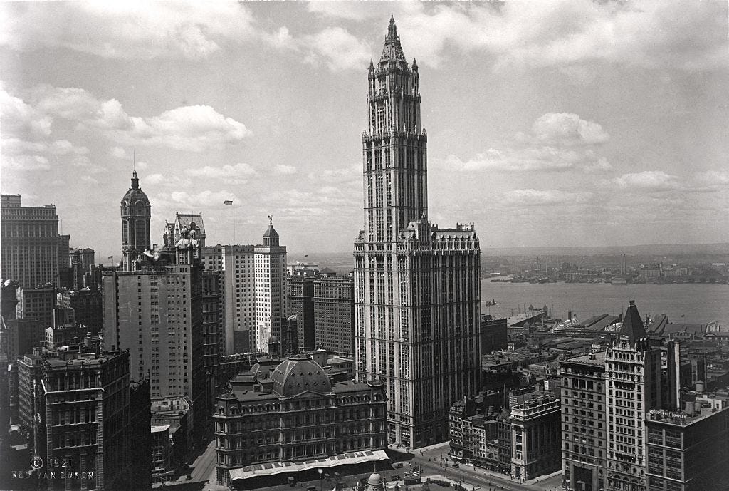 A tall building with a triangular top surrounded by other buildings.