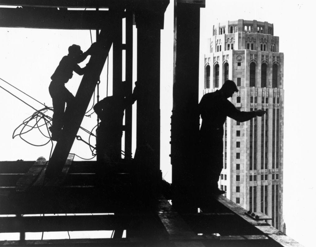 Three men atop a tall building are helping complete its construction.