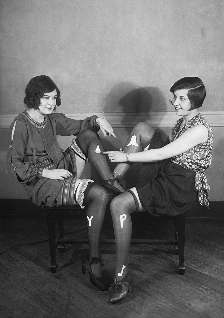 Two women with bobbed hair and similar stockings sit facing each other.