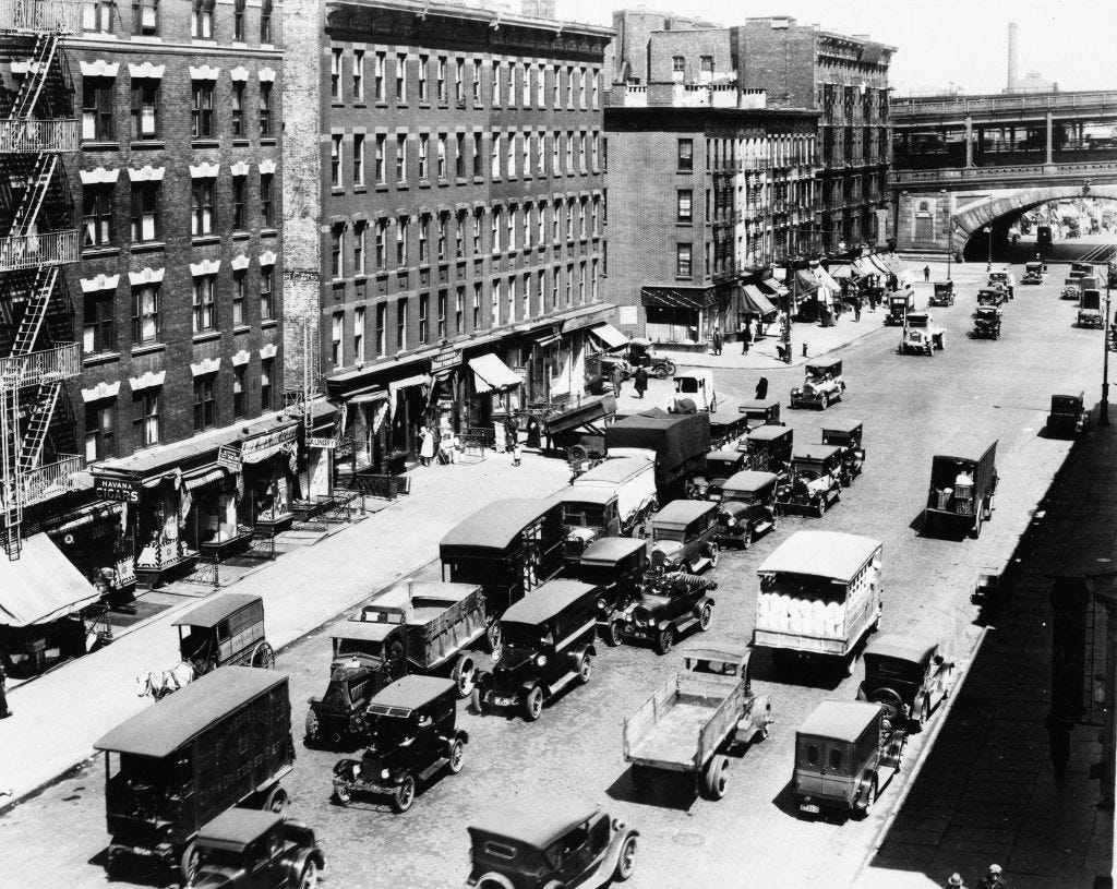 A road in Manhattan with buildings on one side and cars driving past them on another.