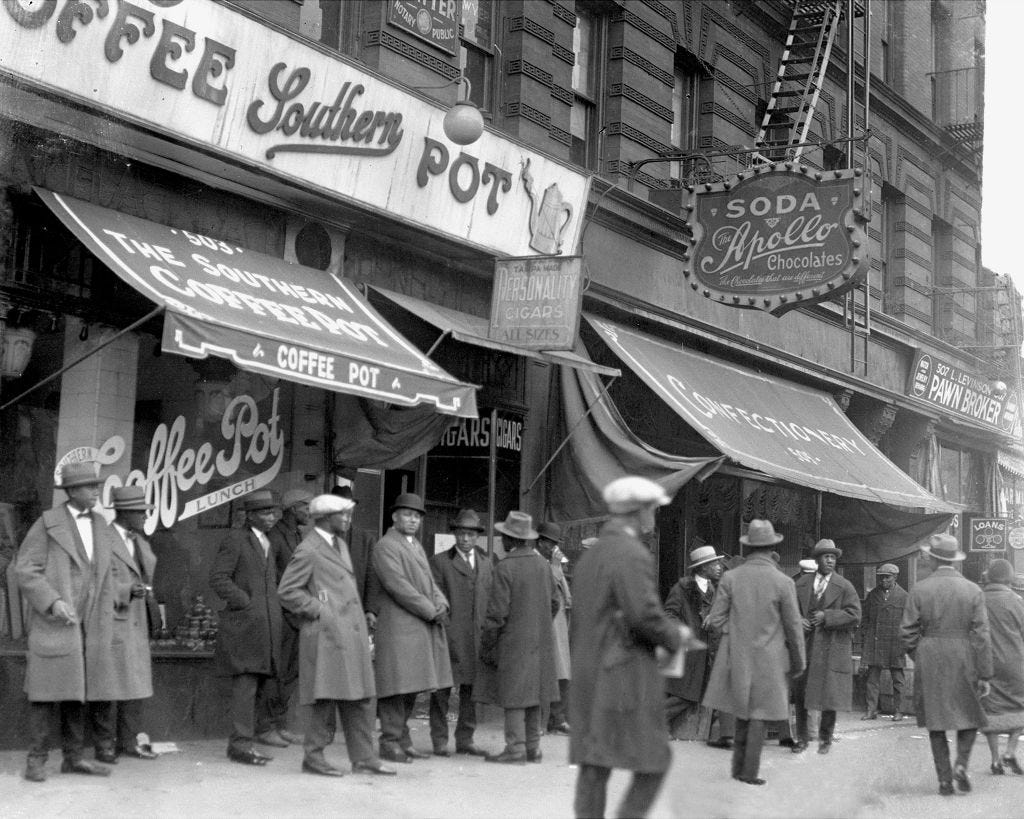 Many people are walking around the streets of Harlem, while some others wait outside the coffee shop. There are three shops, starting with a coffee place, a confectionary, and a pawnbroker.