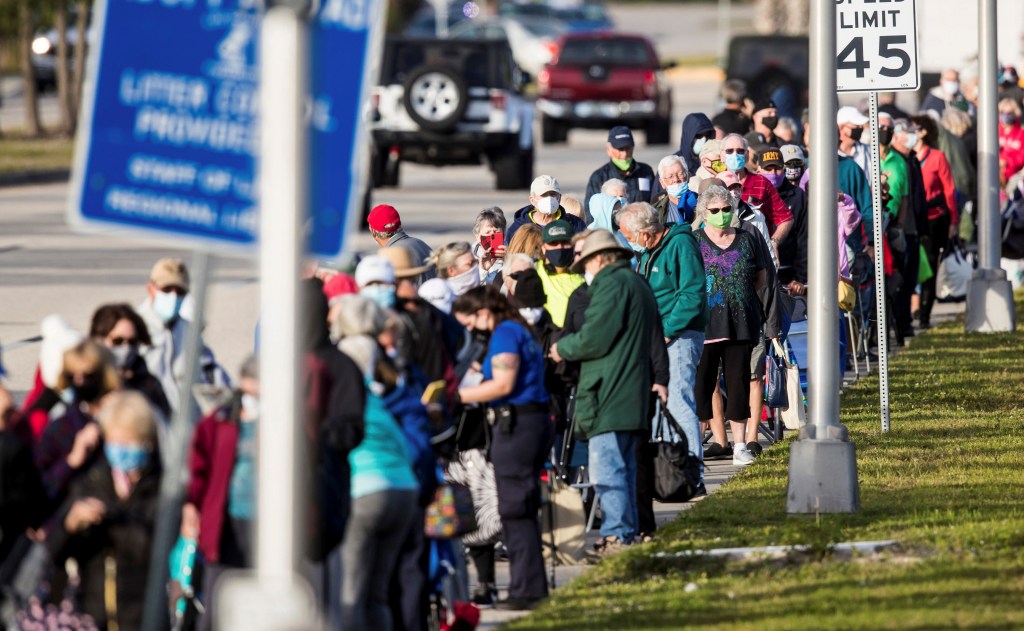 Long line of people wearing masks waiting to receive the COVID-19 vaccine.