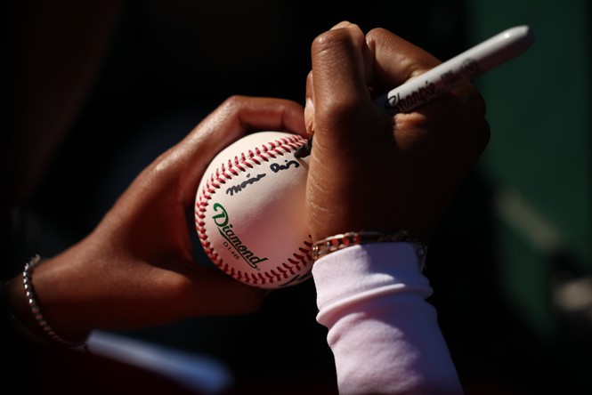 a color photograph of a woman's hands signing a baseball