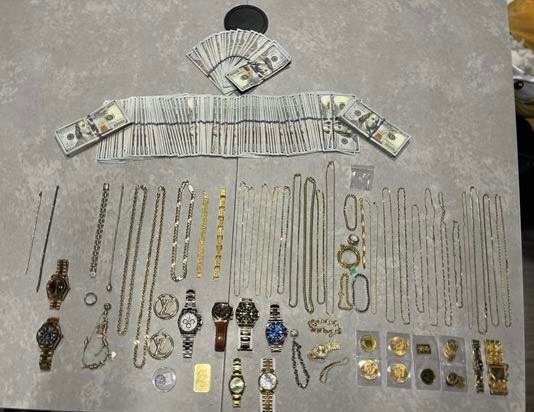 Stacks of cash and numerous gold chains, watches, and other jewelry.