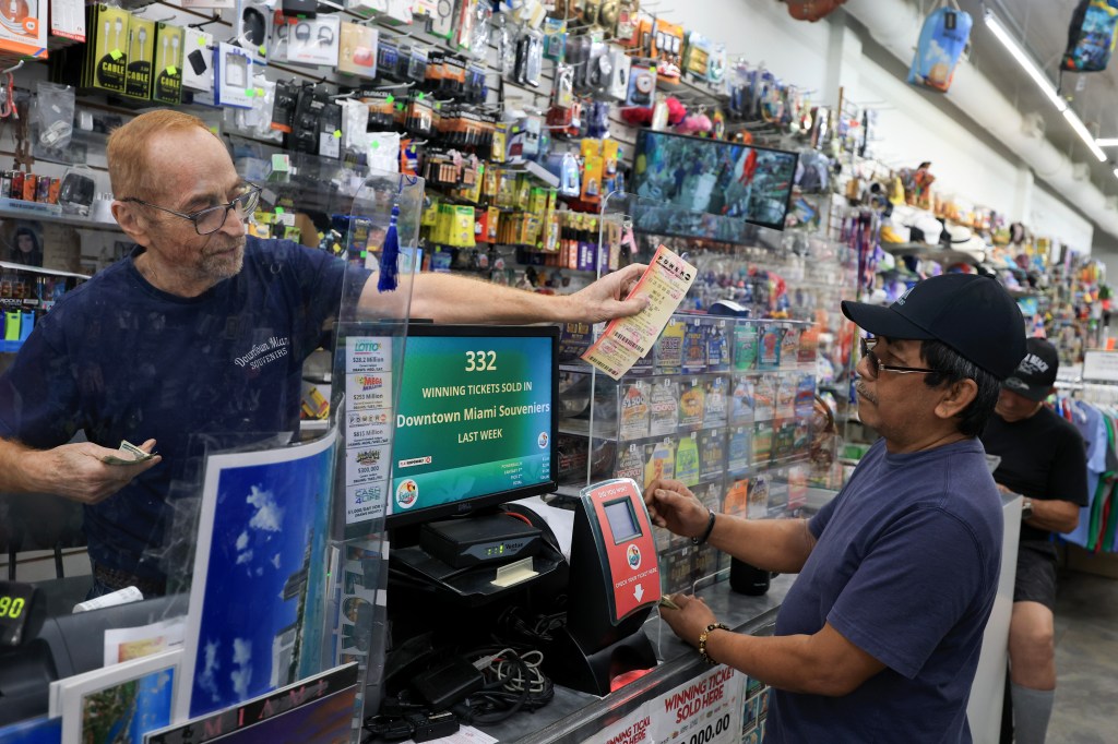 A Miami store worker hands Powerball tickets to a customer on Aug. 26, 2025.