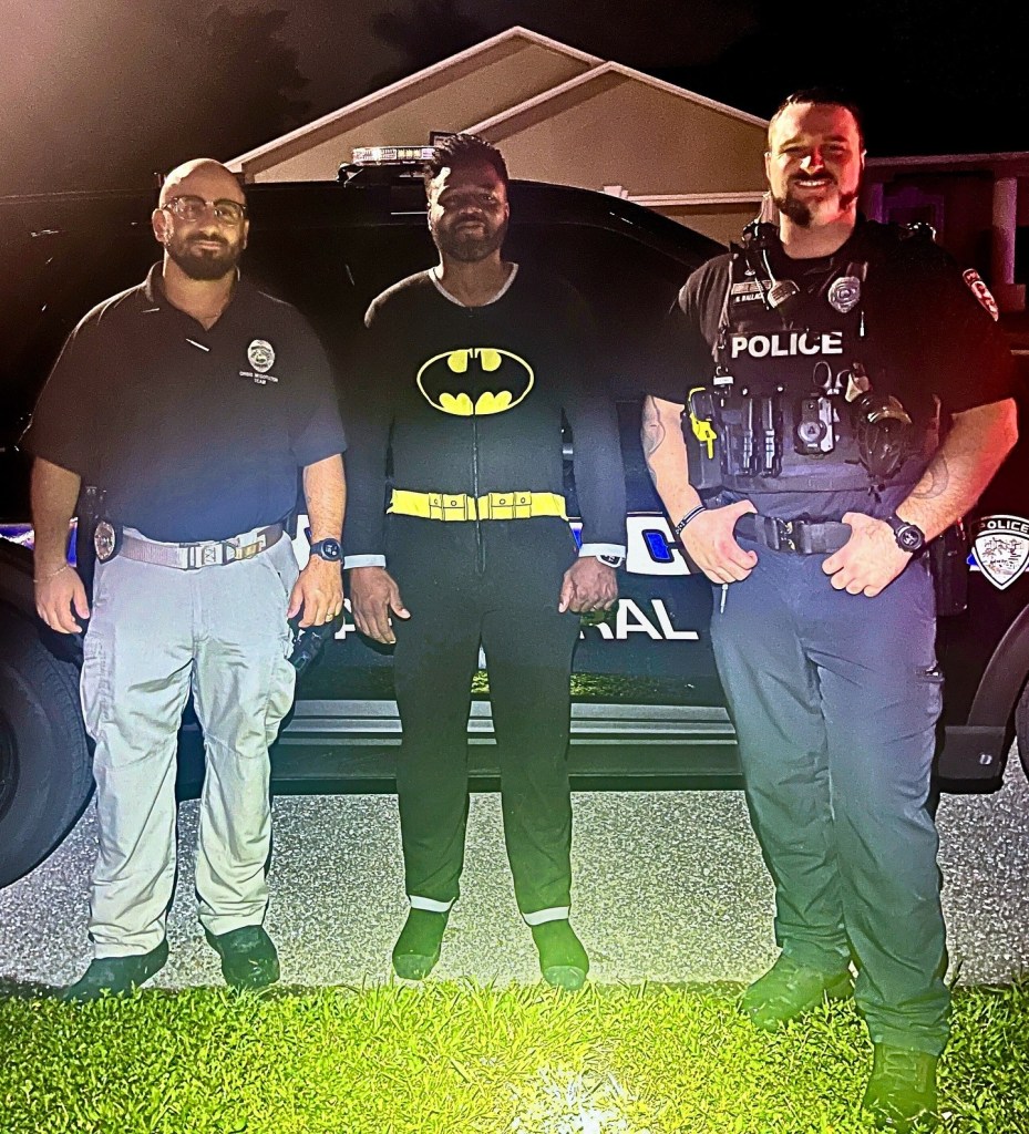 Man in Batman pajamas flanked by two police officers.
