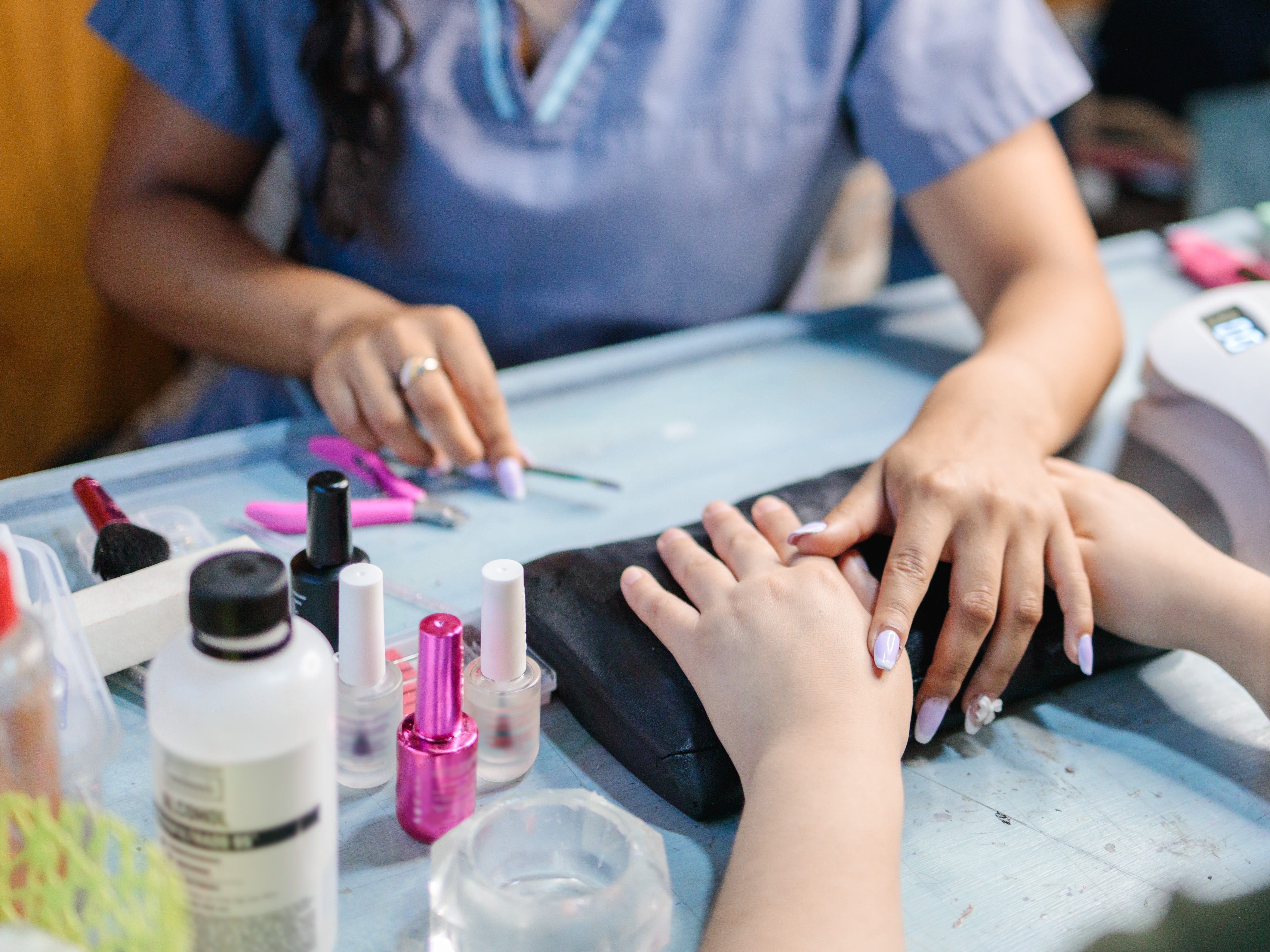 A nail artist doing a client's nails on a workspace with several manicure products on it.