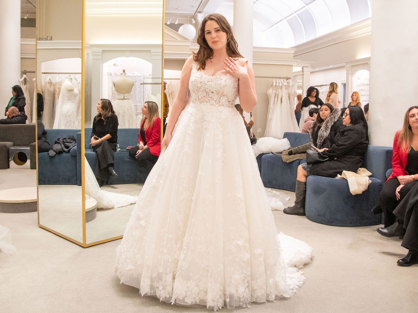A woman stands in a wedding dress in a bridal boutique.