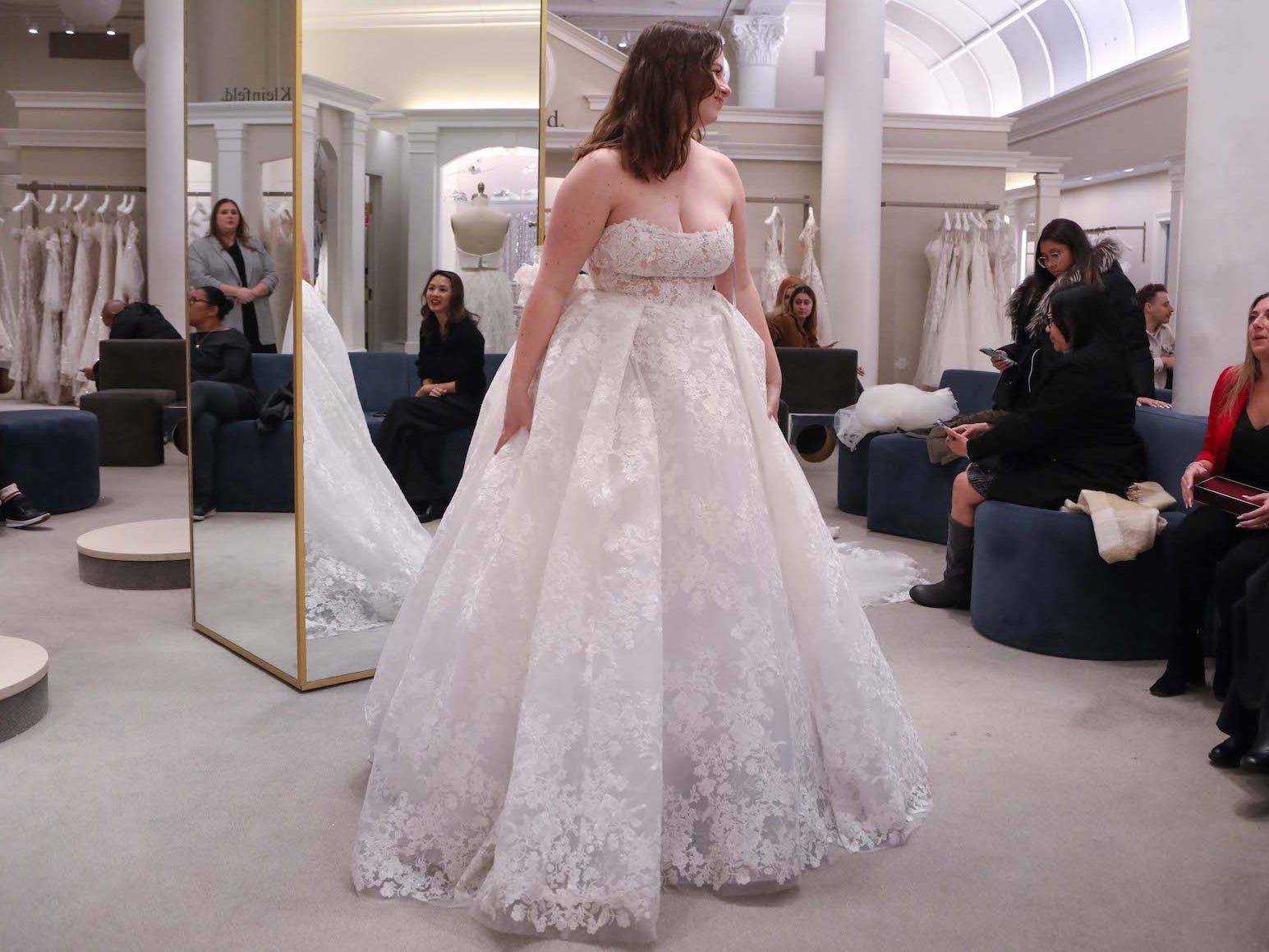 A woman stands in a wedding dress and looks at people sitting on a couch.