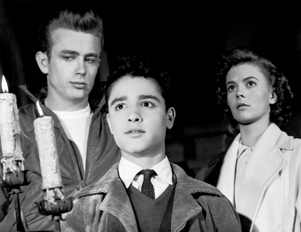 Black and white still image of James Dean, Sal Mineo, and Natalie Wood in *Rebel Without a Cause*.