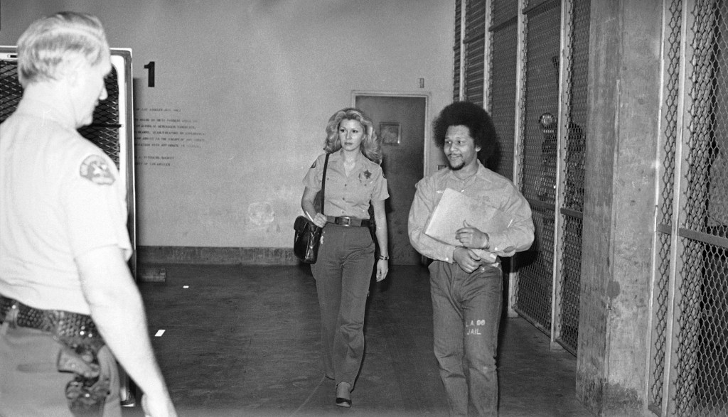Black and white photo of Lionel Williams, escorted by a policewoman, after being found guilty of murdering Sal Mineo.
