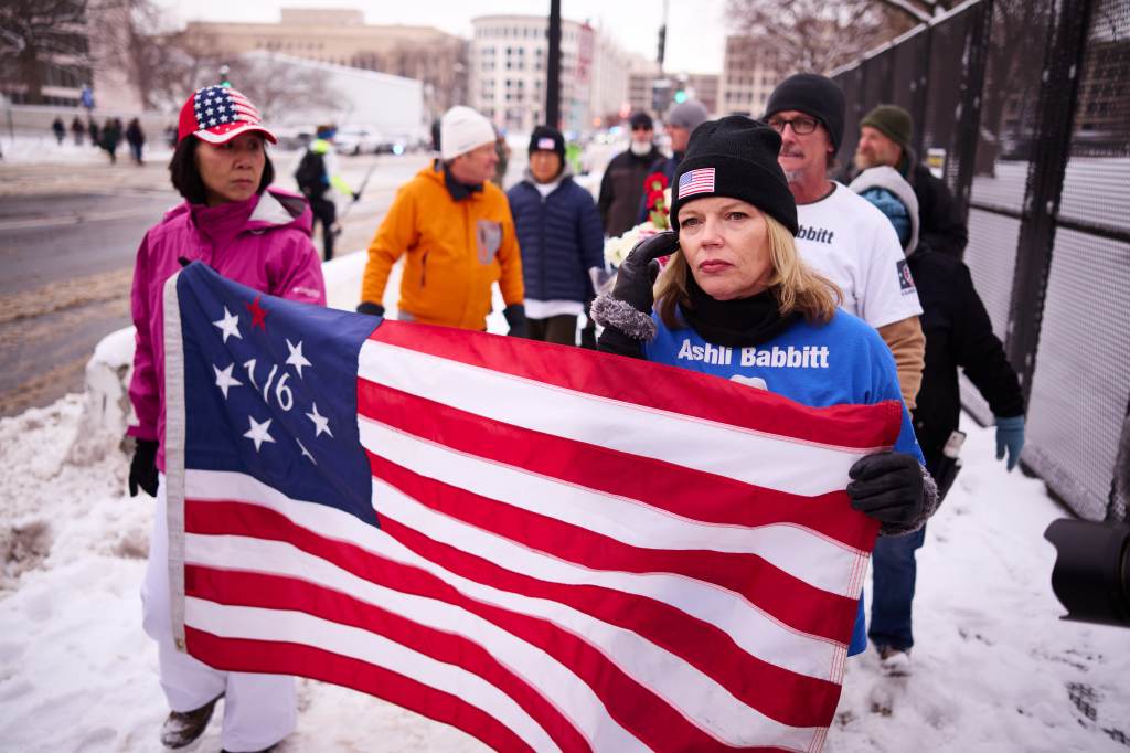 A woman holds a Betsy Ross flag and an Ashli Babbitt shirt at a memorial outside the U.S. Capitol.