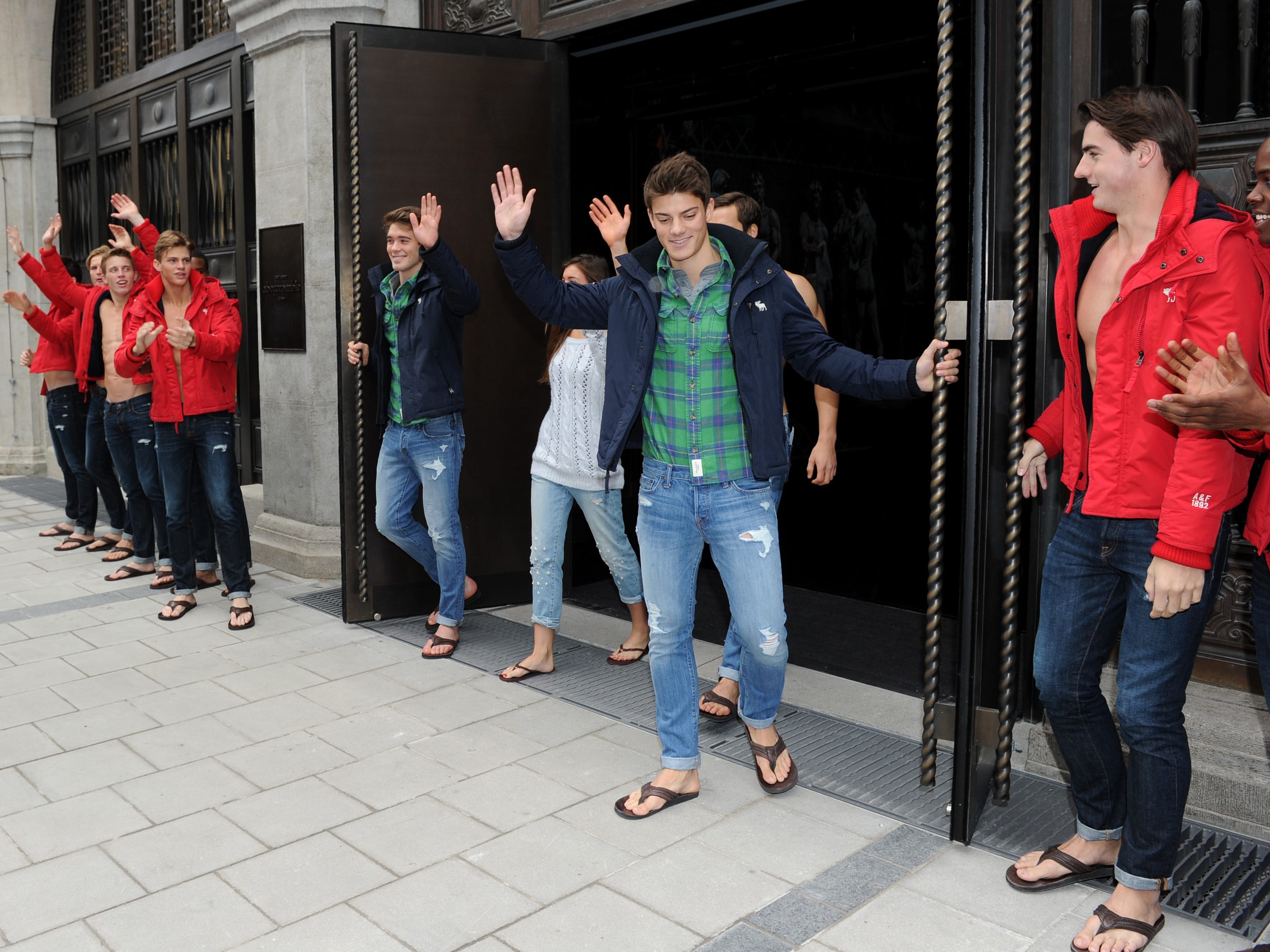 Group of male Abercrombie & Fitch employees open doors of new store while waving
