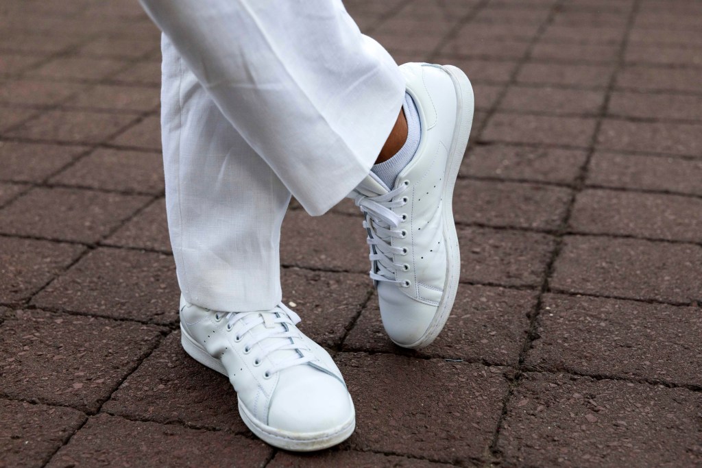 Person's legs and white sneakers on a brick pavement.