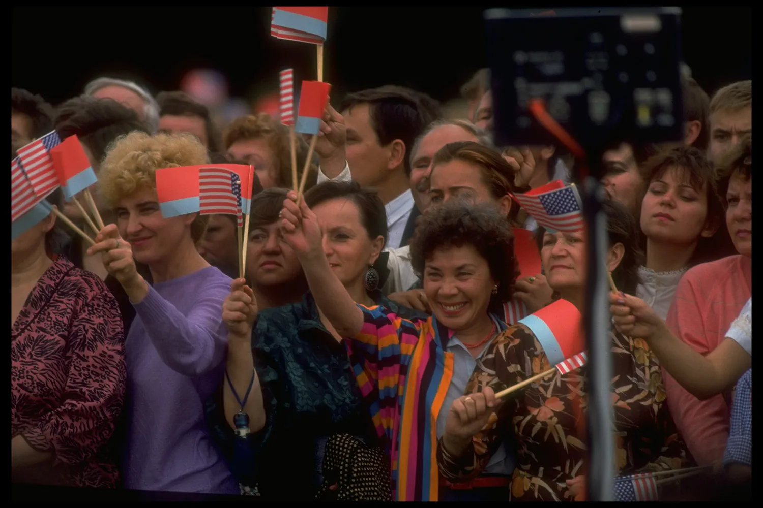 A crowd of people smiling and waving small flags on sticks.