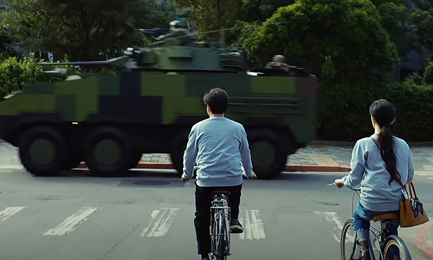 A tank moves toward a man on a bicycle.