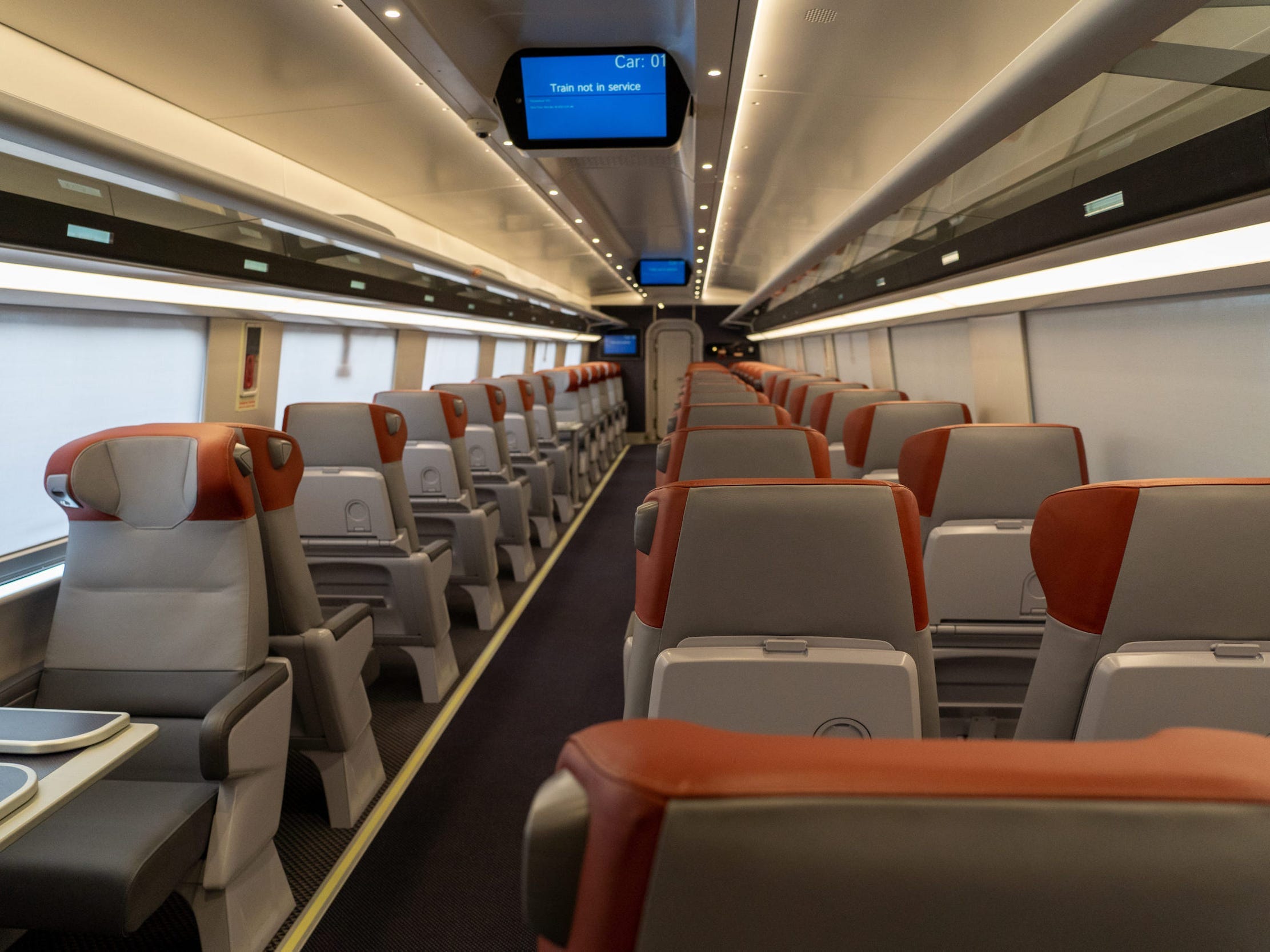 The new Amtrak Acela first class interior with rows of seats with orange headrests and a digital screen.