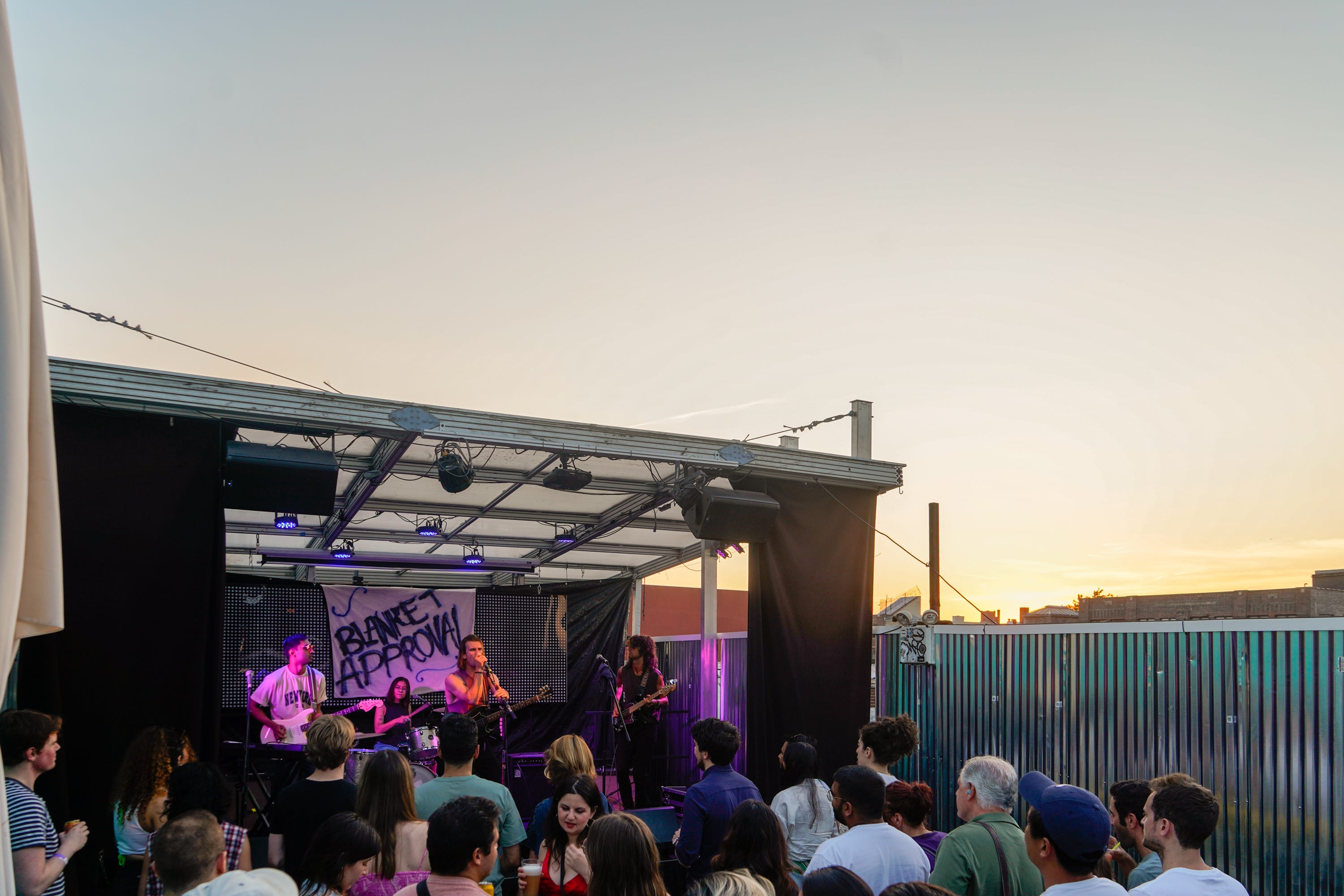 A band plays in front of a crowd on a rooftop at sunset