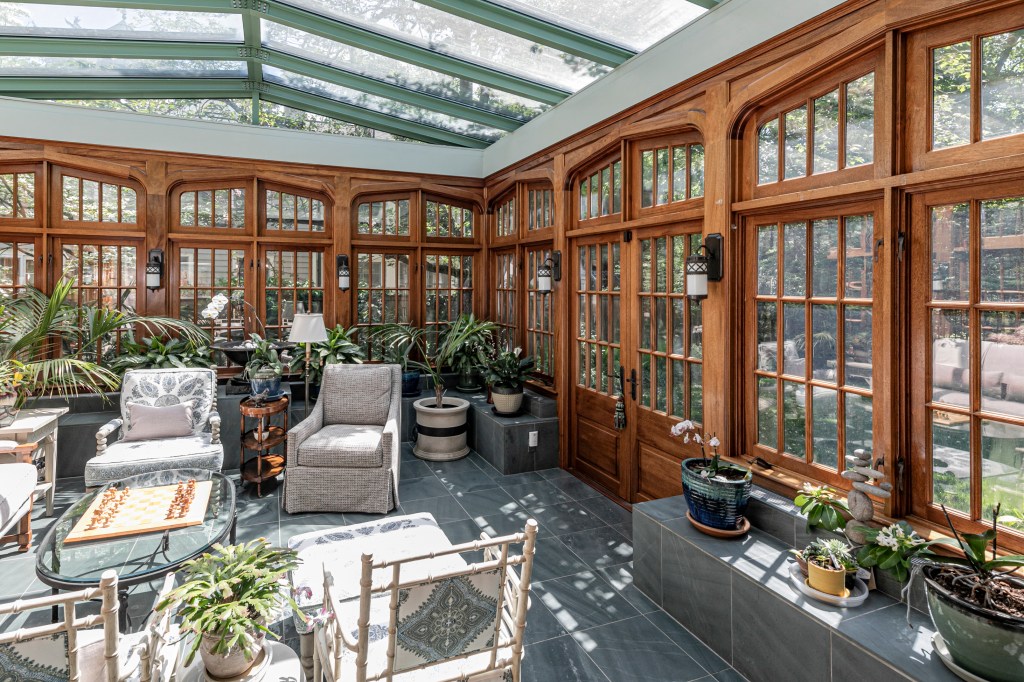 Sunroom with wood-framed windows, glass ceiling, and plants.