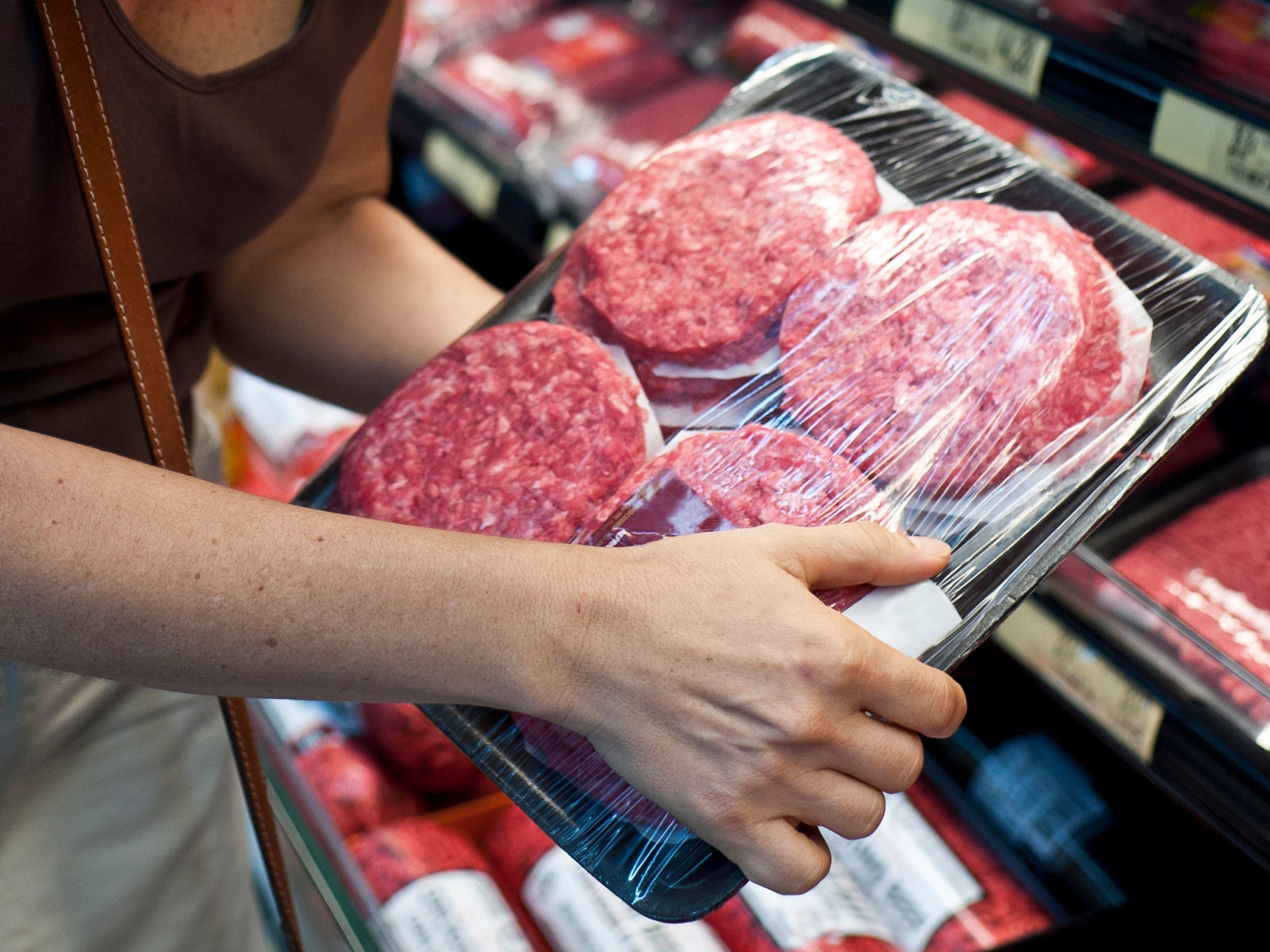 person holding fresh burger patties in grocery store