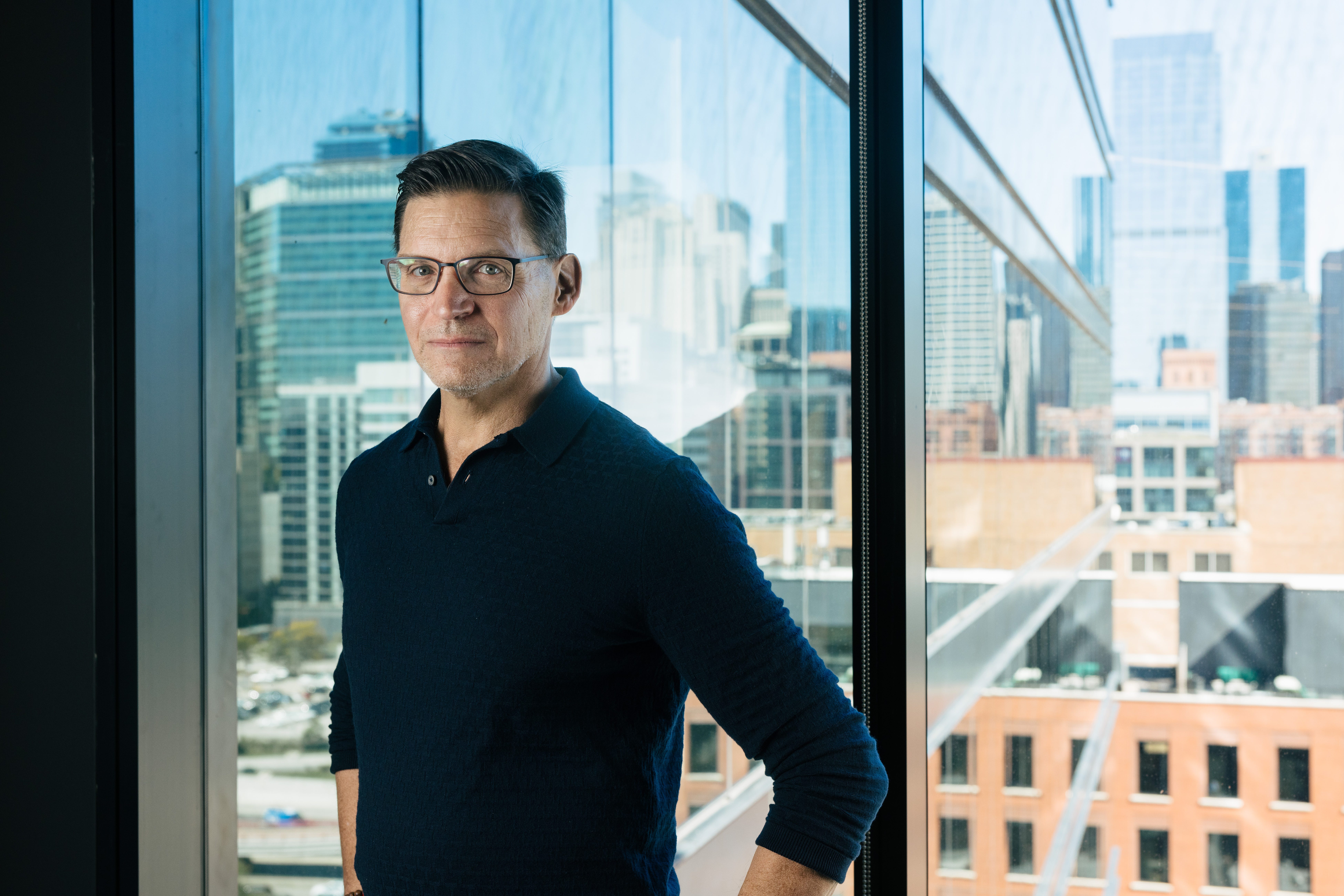 headshot of a man in a dark shirt in front of a city view