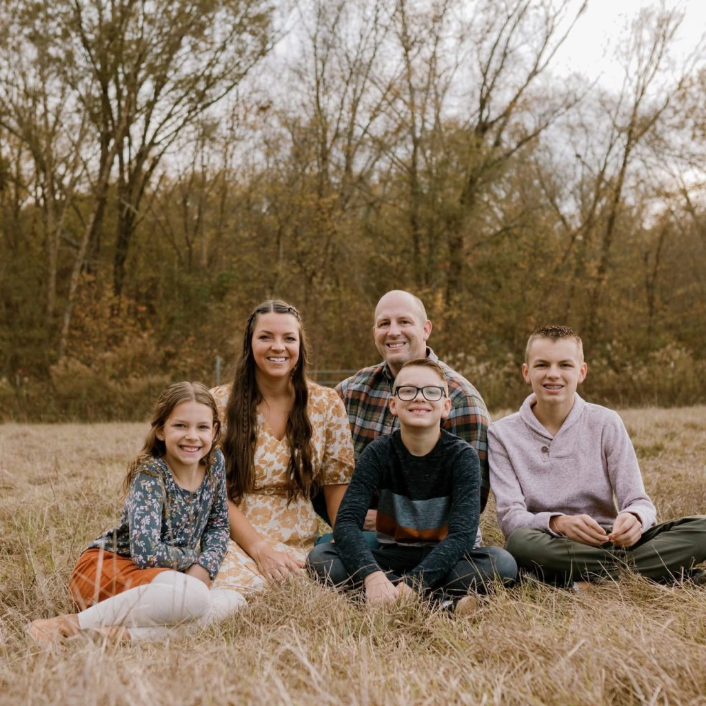 The Colton family, a mother, father, and their three children, sitting together in a field.