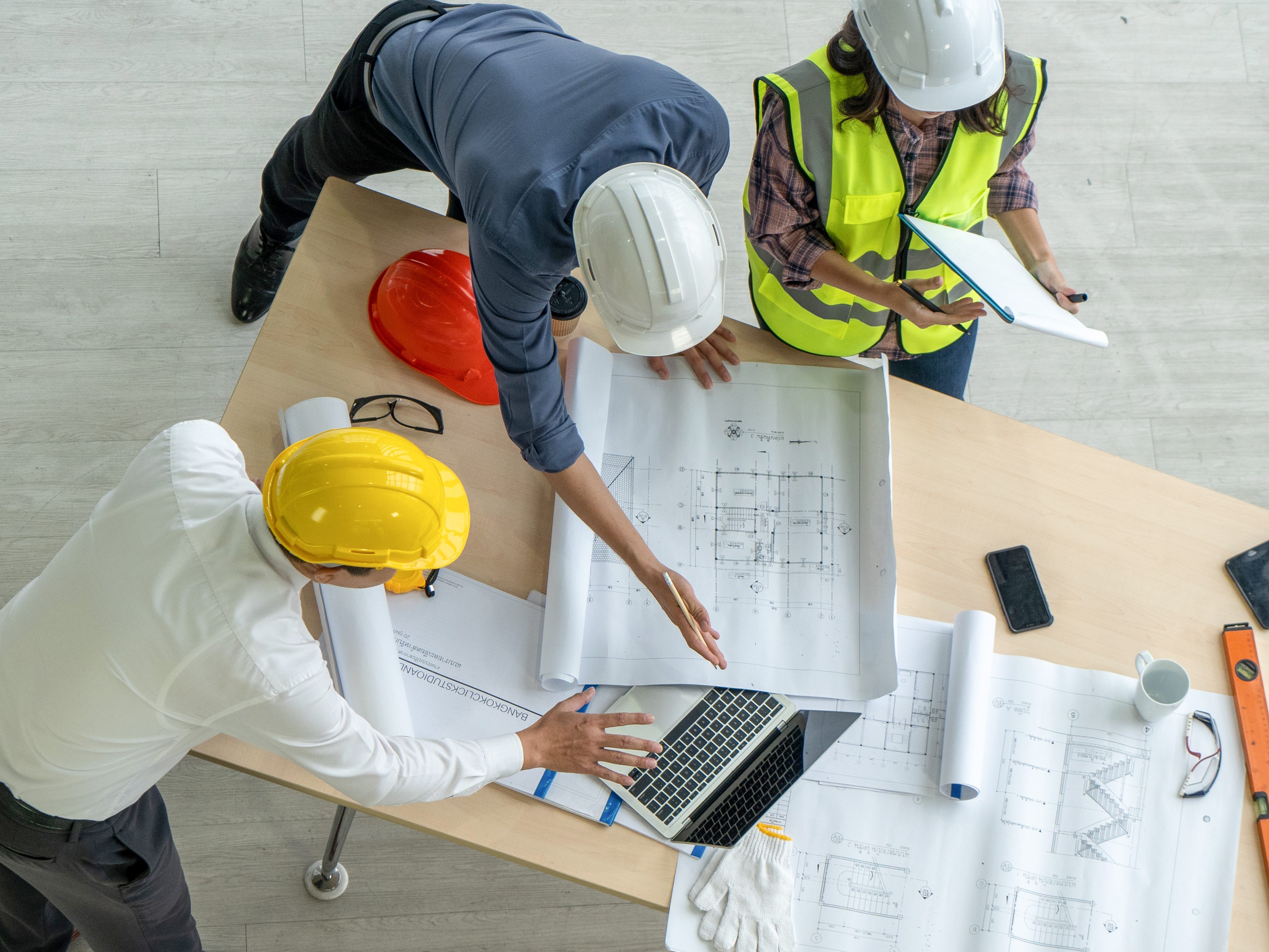 Three people with hard hats working at a table at a construction site