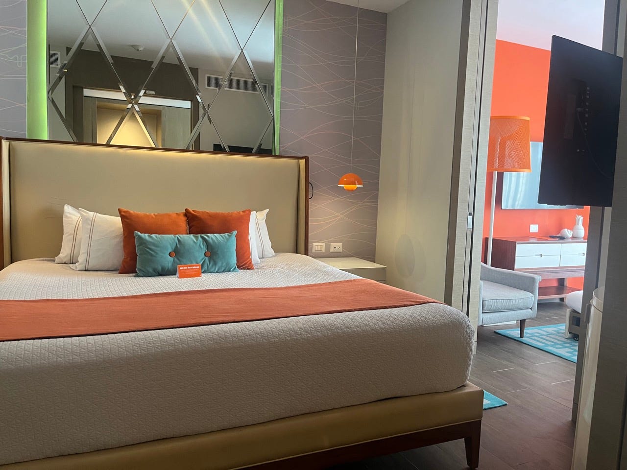 Room with beige headboard, orange pillows, large bed with nightstand next to it