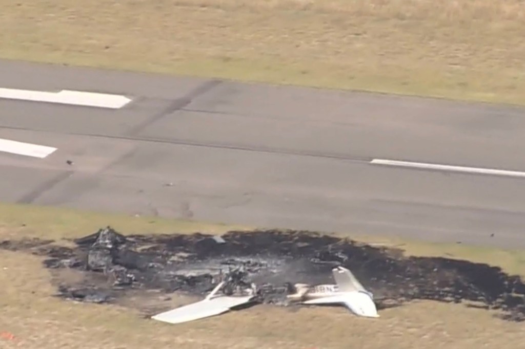 Burned plane wreckage on a runway.