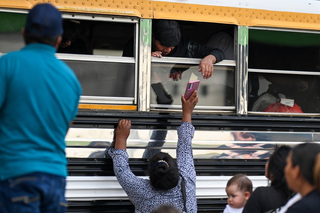 A Guatemalan migrant deported from the US shows a cellphone to a family member outside a bus.