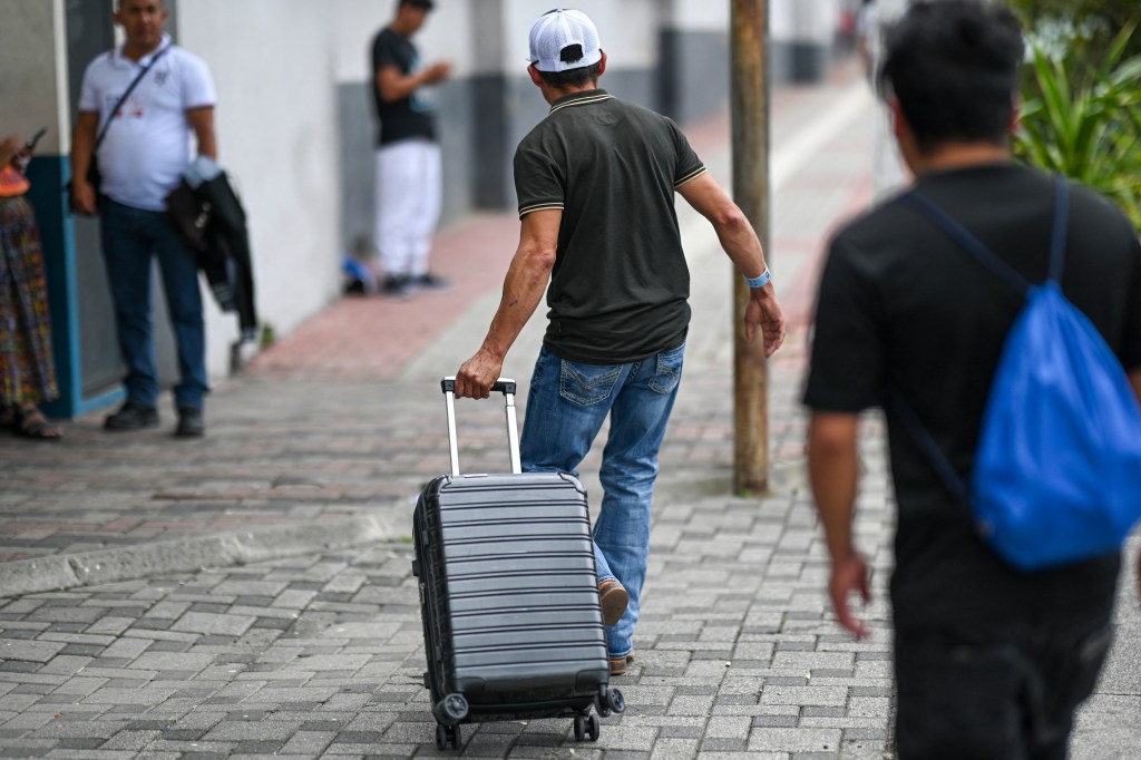 A Guatemalan migrant, deported from the U.S., walks away from the camera pulling a suitcase.