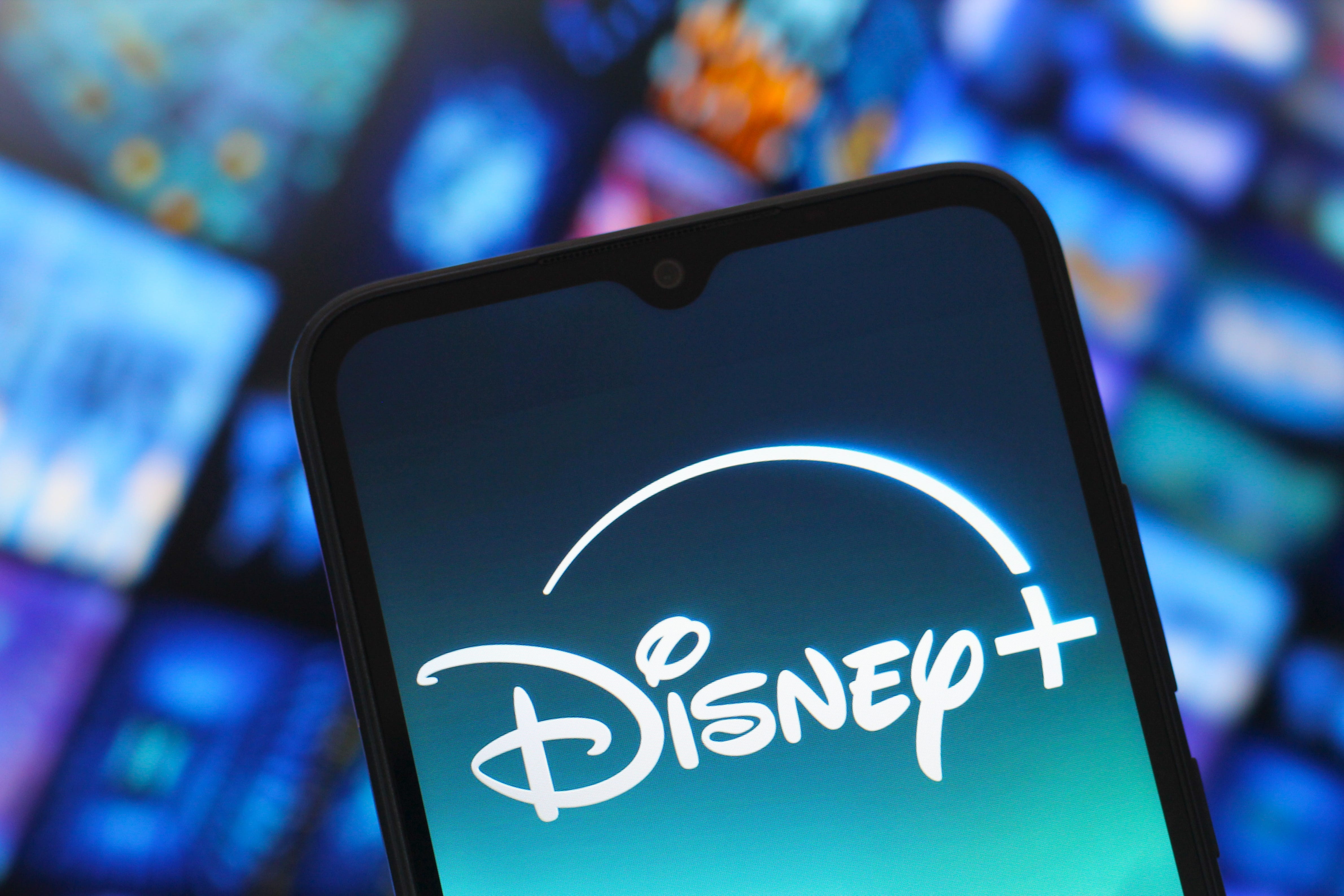 The Disney Plus logo is displayed on a smartphone screen against a blurred screen background.