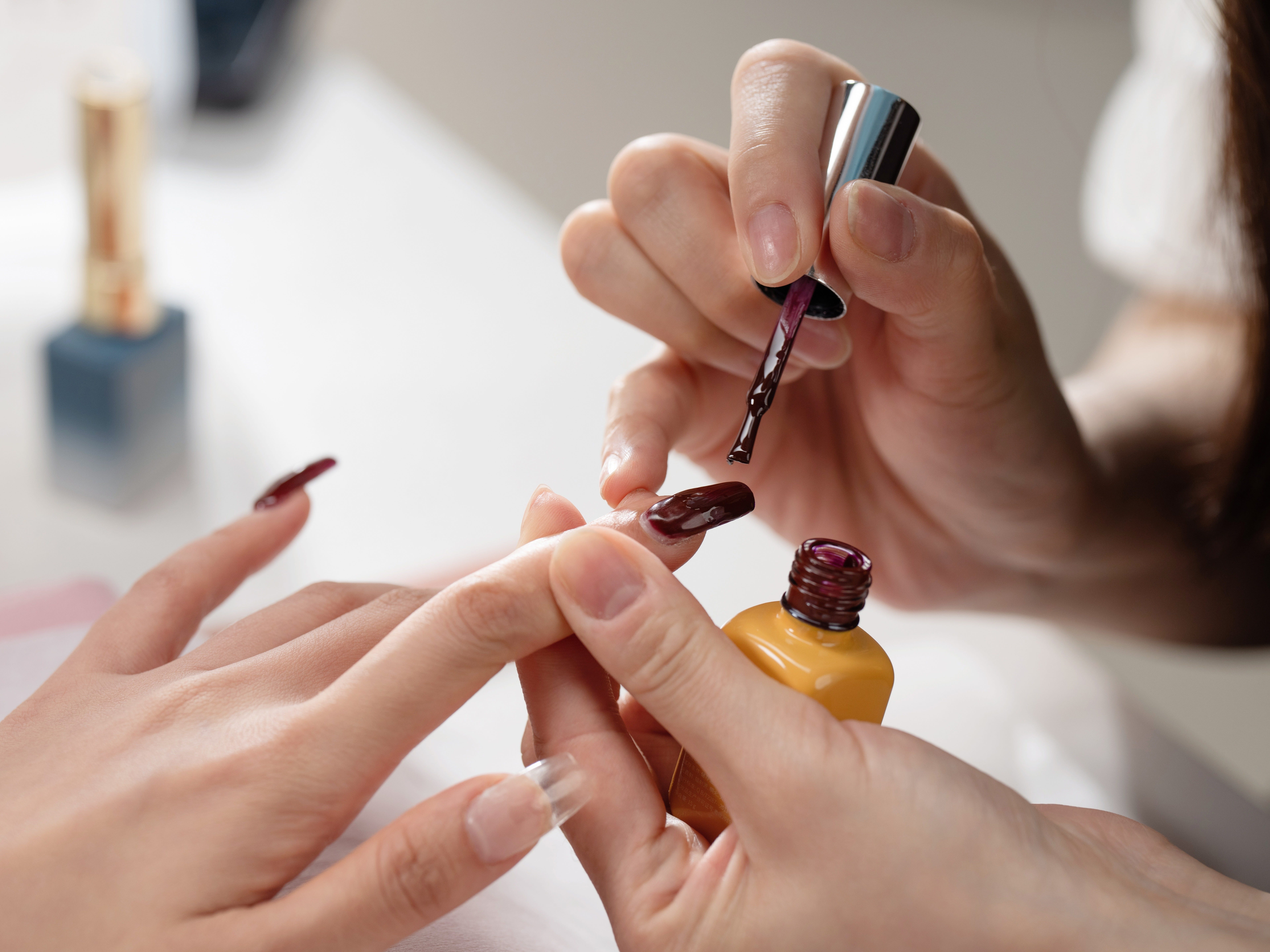A nail technician painting someone's nails a deep purple color.