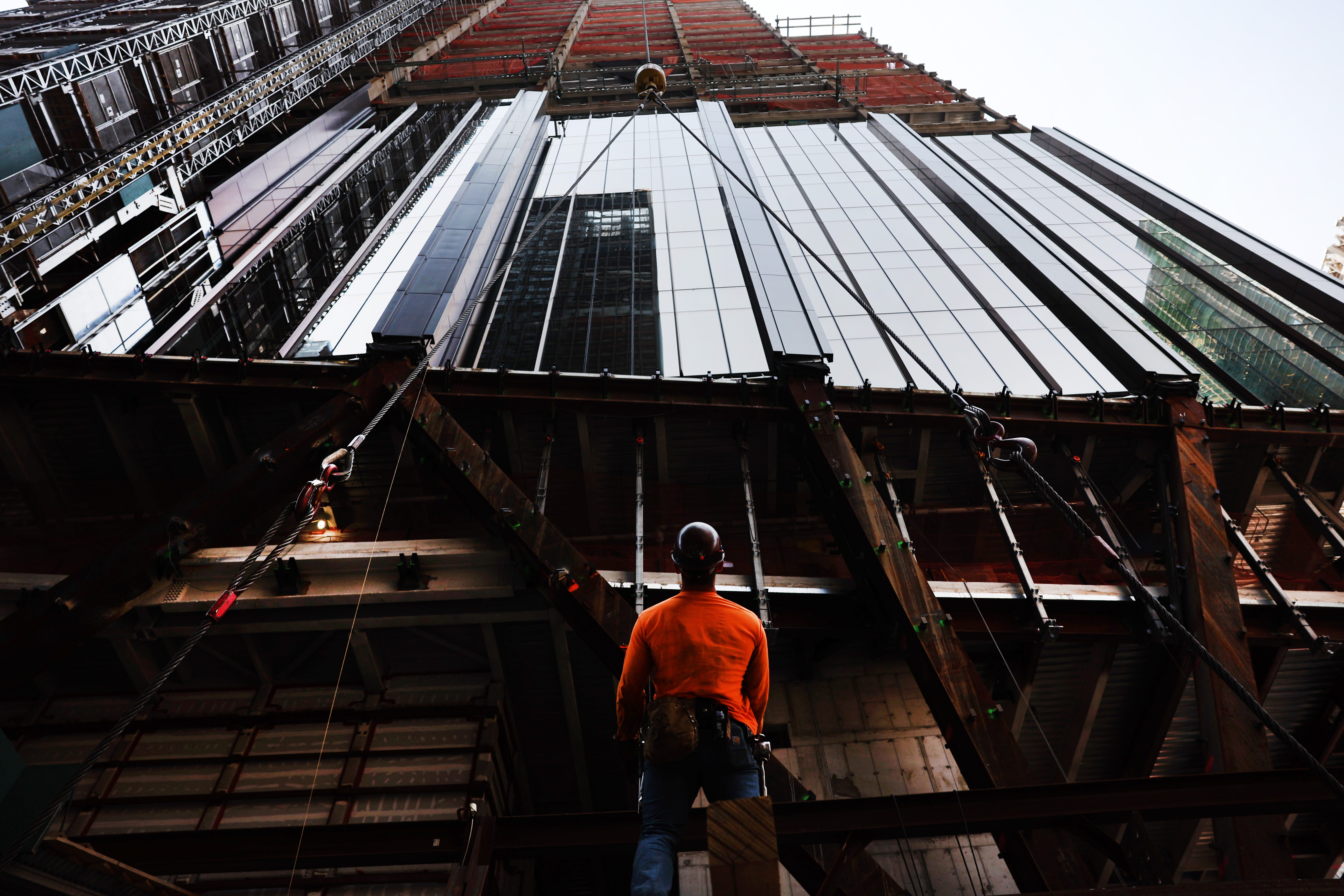 A construction worker looks up at a skyscraper