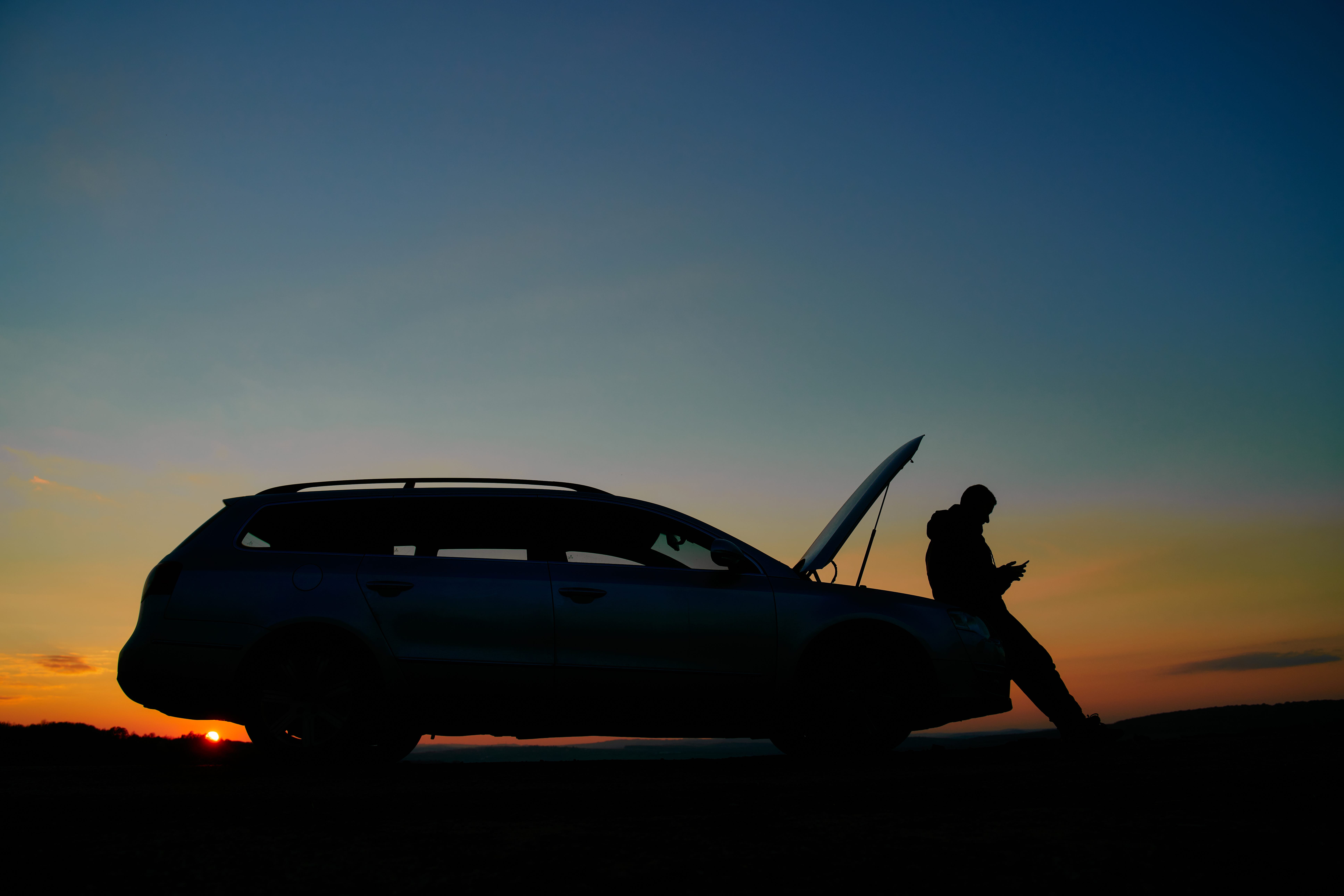 A man stands alone by his car on the side of the road.