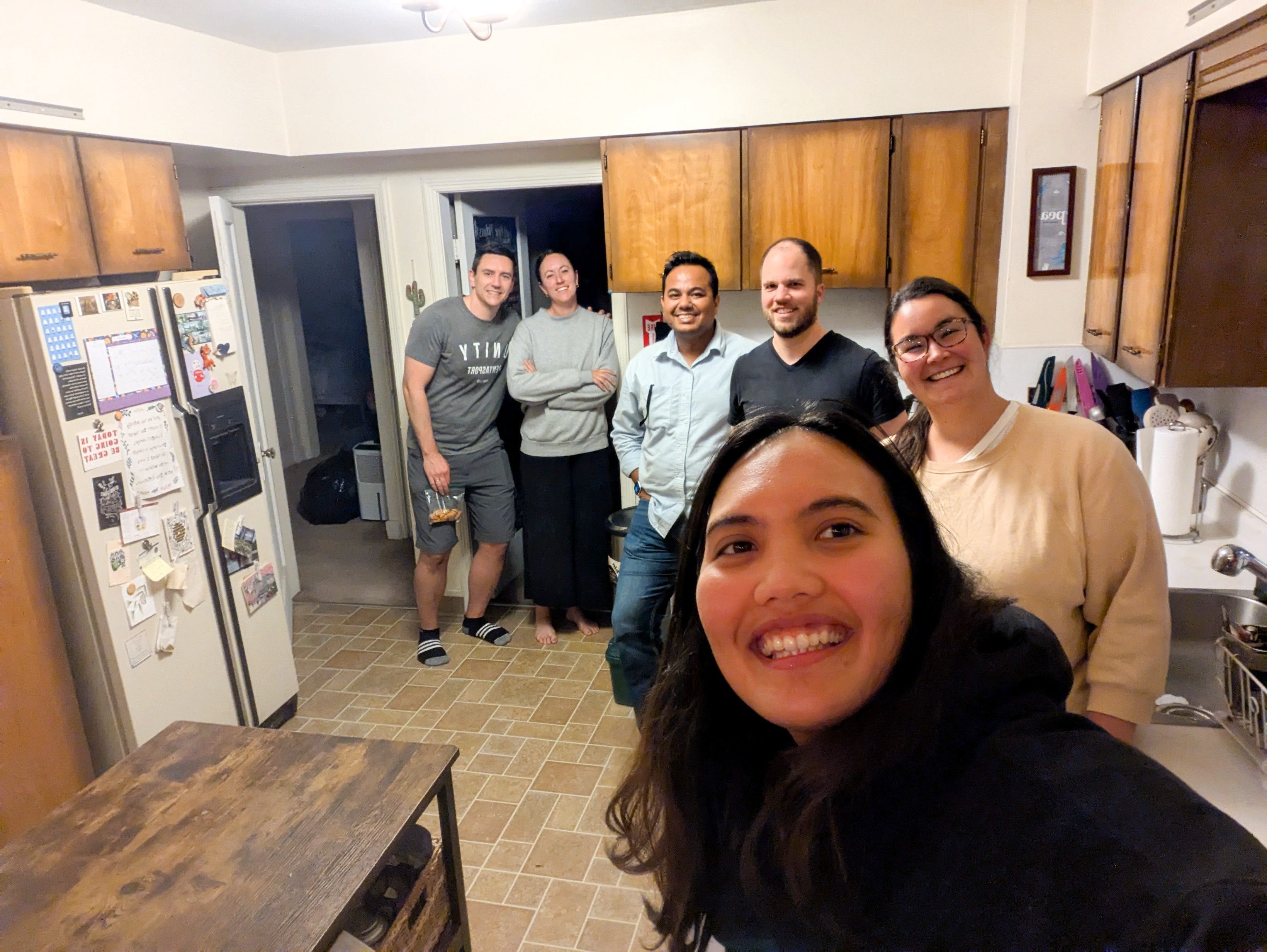 The writer (far right behind the selfie taker wearing a light tan sweater) is posing for a photo with her five roommates in their kitchen.